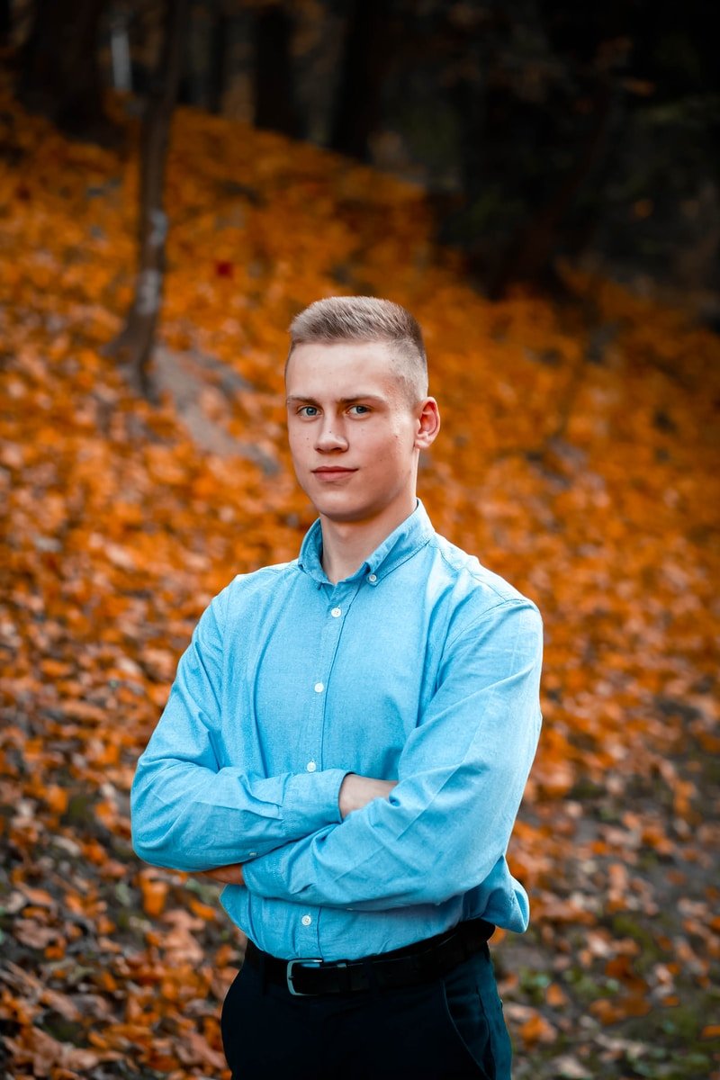 man in blue dress shirt standing on brown leaves during daytime